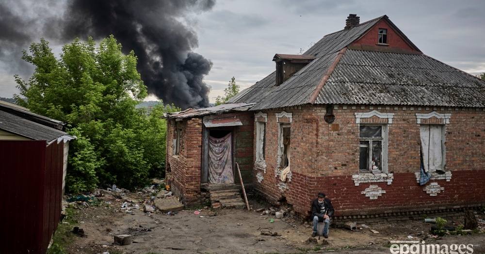 Местный житель сидит возле своего поврежденного дома на фоне столба дыма, поднимающегося после обстрела, на окраине Харькова, 17 мая 2024 / Фото EPA. Сергей Козлов
