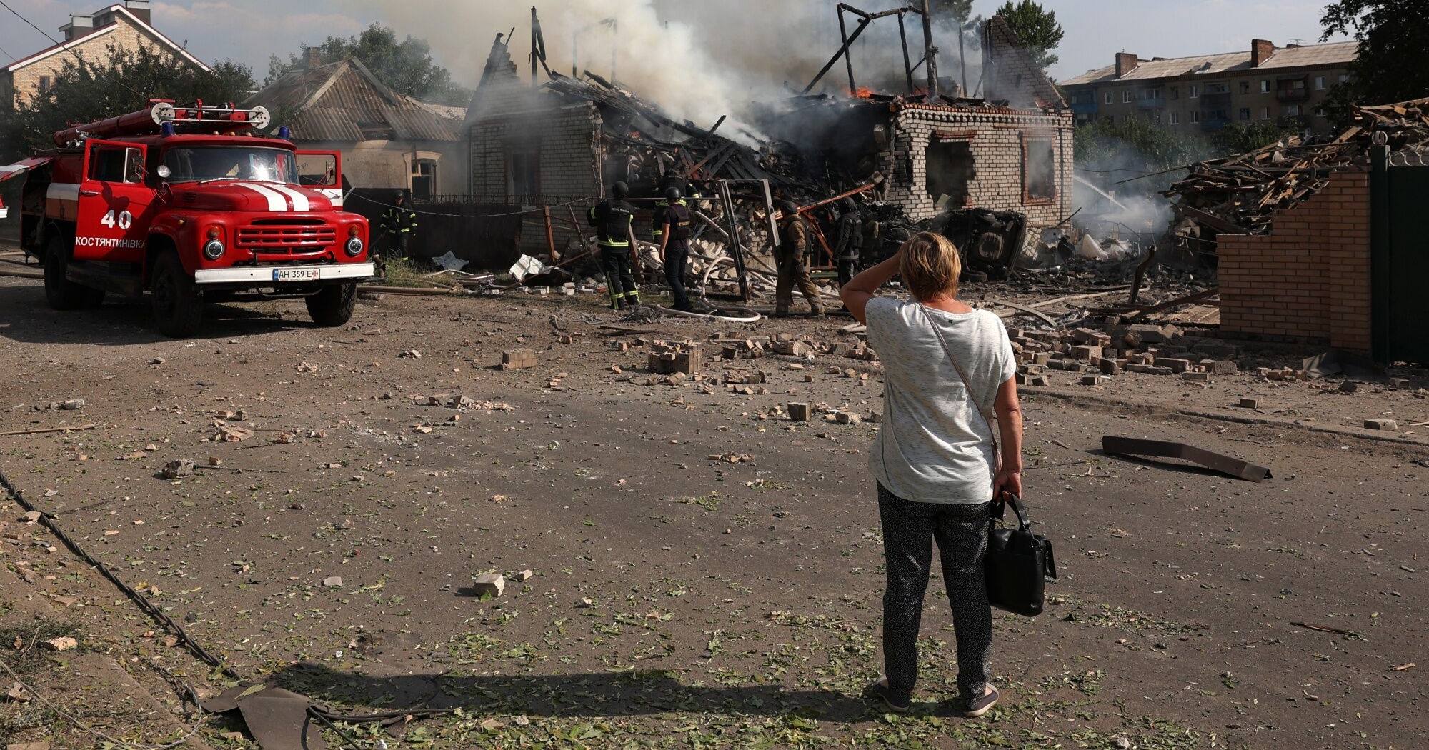 Местная жительница наблюдает за спасателями, которые тушат пожар в доме, разрушенном во время ракетного обстрела в городе Константиновка Донецкой области 21 июля 2024 / Фото AFP