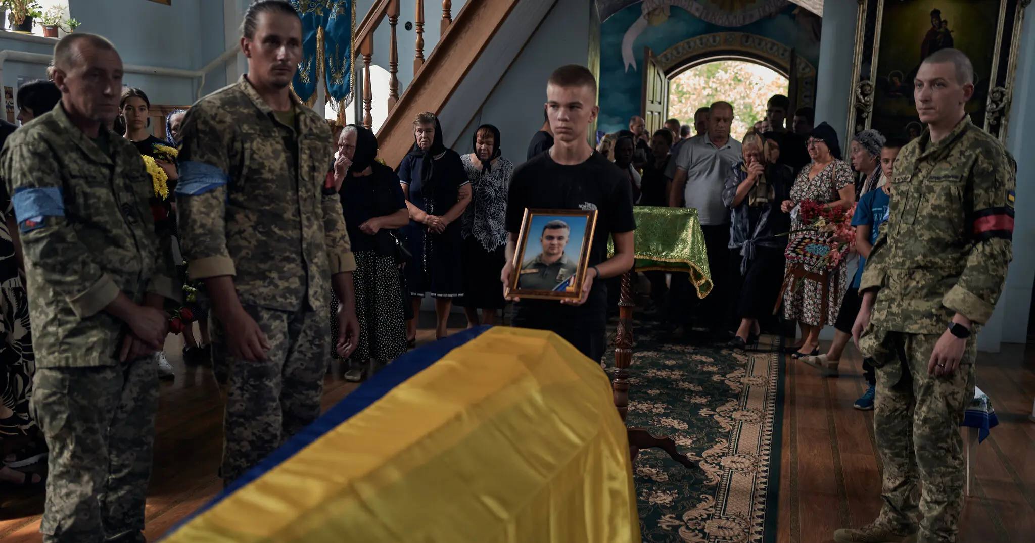 Сын Алексея Меся, украинского пилота F-16, держит фотографию отца во время похорон полковника в четверг в Шепетовке / Фото NYT