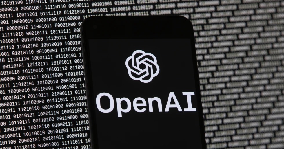 Логотип OpenAI на мобільному телефоні перед екраном комп'ютера з випадковими двійковими даними / Фото AP Photo
