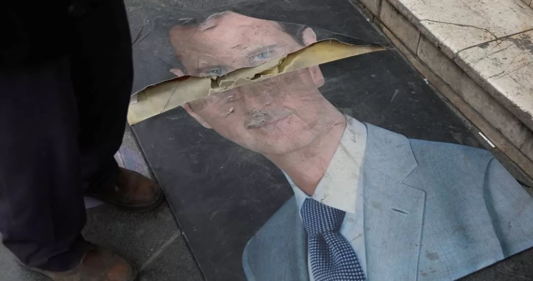 Людина стоїть біля пошкодженої фотографії Башара Асада в Дамаску / Фото: REUTERS