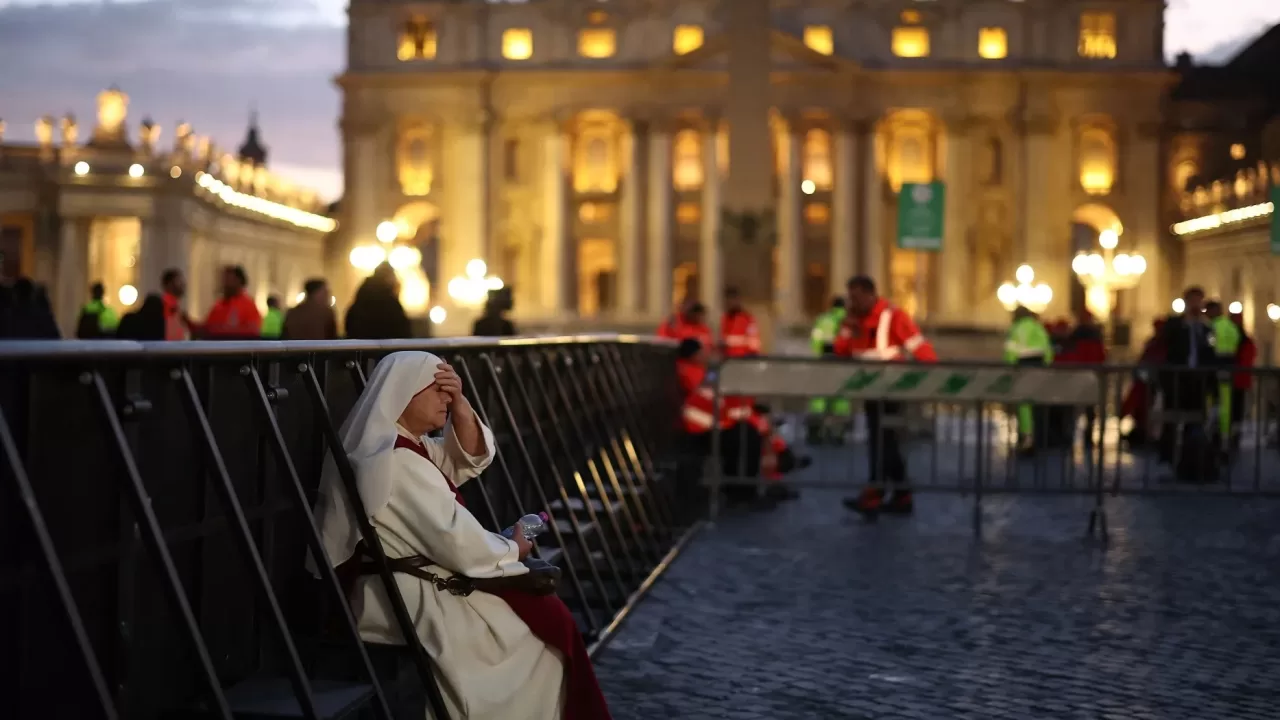 Монахиня сидит на ограде перед базиликой Святого Петра в Ватикане 25 апреля / Фото AFP