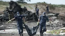 Українські працівники рятувальних служб несуть тіло жертви, поки російські бойовики стоять на варті на місці катастрофи рейсу MH17 Malaysia Airlines, 20 липня 2014 року / Фото: AP