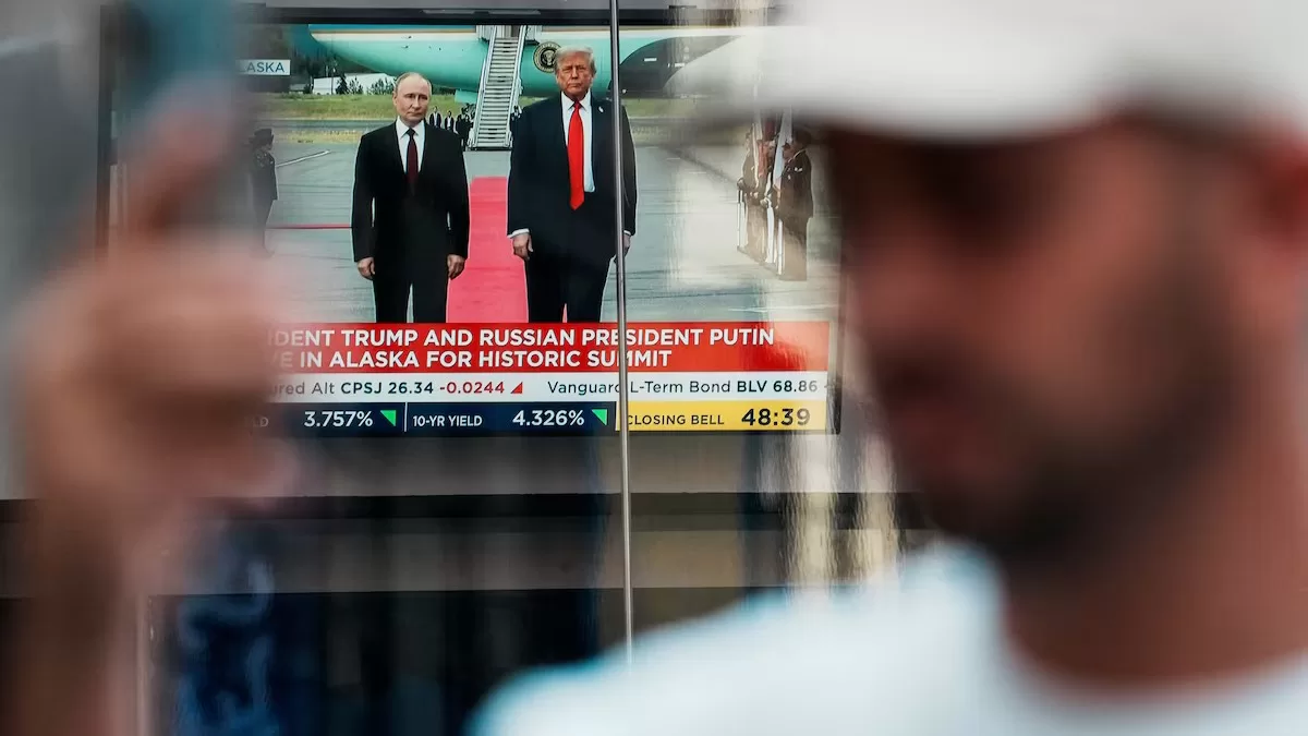 A person walks past a screen showing Trump's meeting with Putin in Alaska on 15 August 2025 / Photo: Reuters