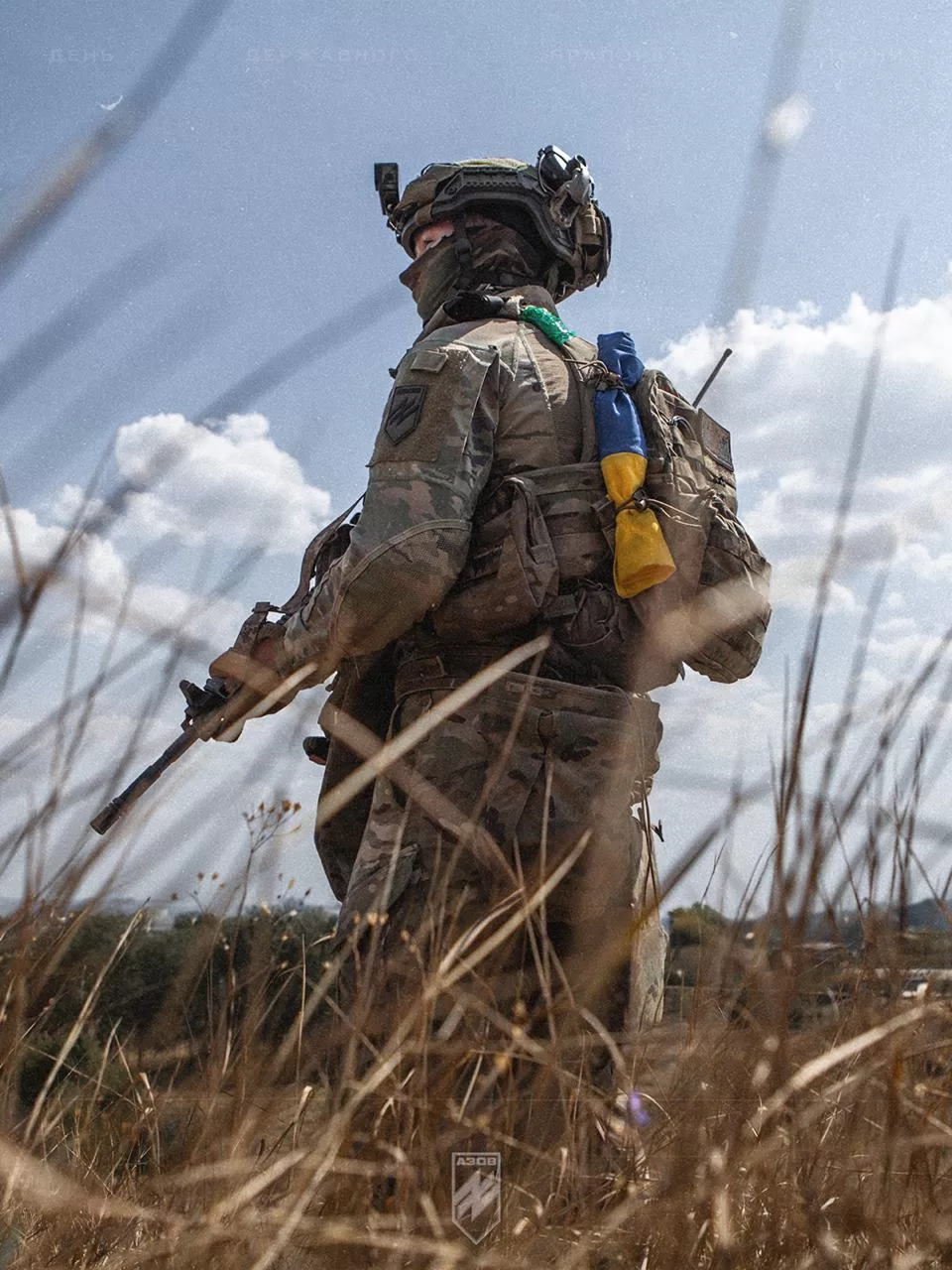 Споряджений боєць стоїть серед поля, тримаючи гвинтівку