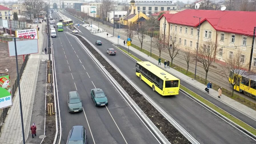Широка відремонтована вулиця у Львові з кількома смугами руху. Посередині їде жовтий міський автобус, поруч рухаються автомобілі. Праворуч видно трамвайну колію, тротуар із пішоходами та будівлі з червоними дахами. Удалині — будівля головного залізничного вокзалу / Фото: Львівська міська рада