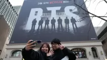 Пара робить селфі біля банера, що рекламує концерт BTS на площі Кванхвамун в Сеулі / Фото AP Photo