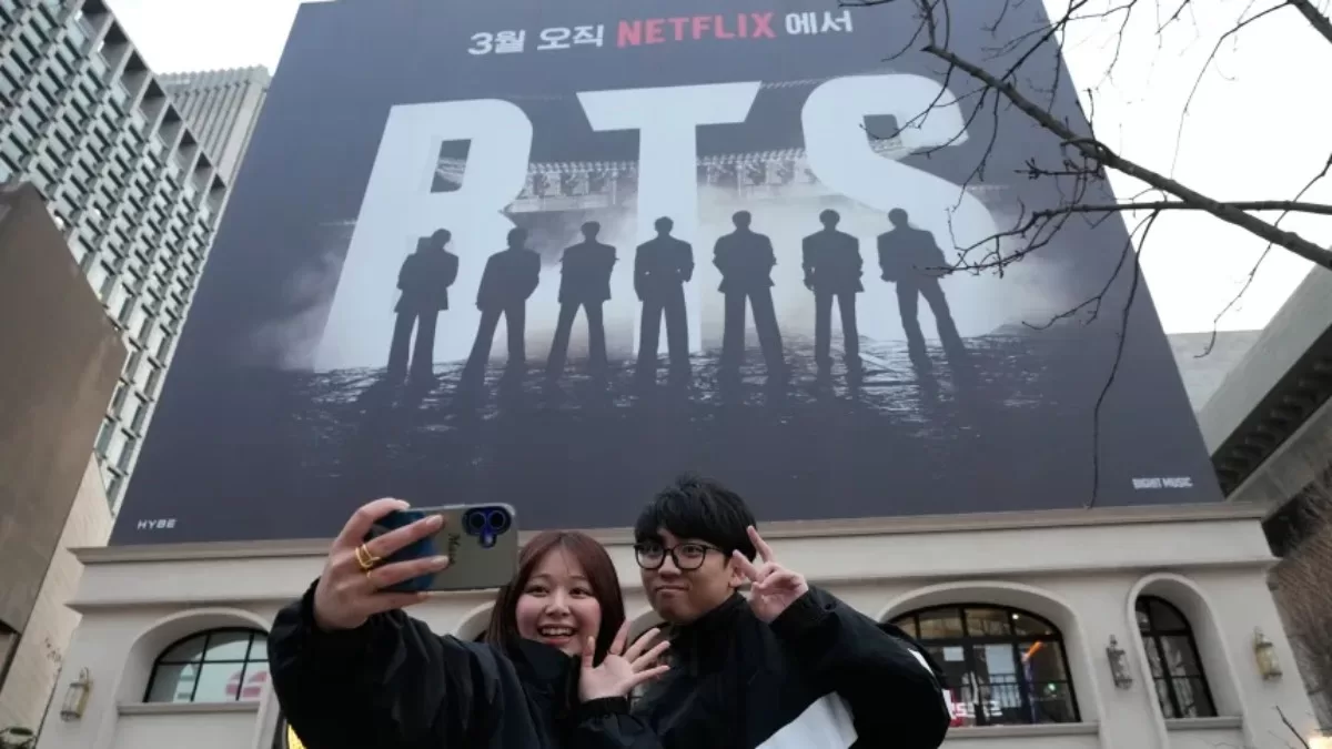 Пара робить селфі біля банера, що рекламує концерт BTS на площі Кванхвамун в Сеулі / Фото AP Photo