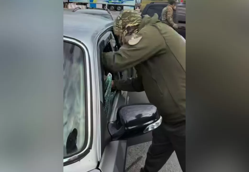 Чоловік в однострої поряд з автівкою з розбитим склом / Скриншот