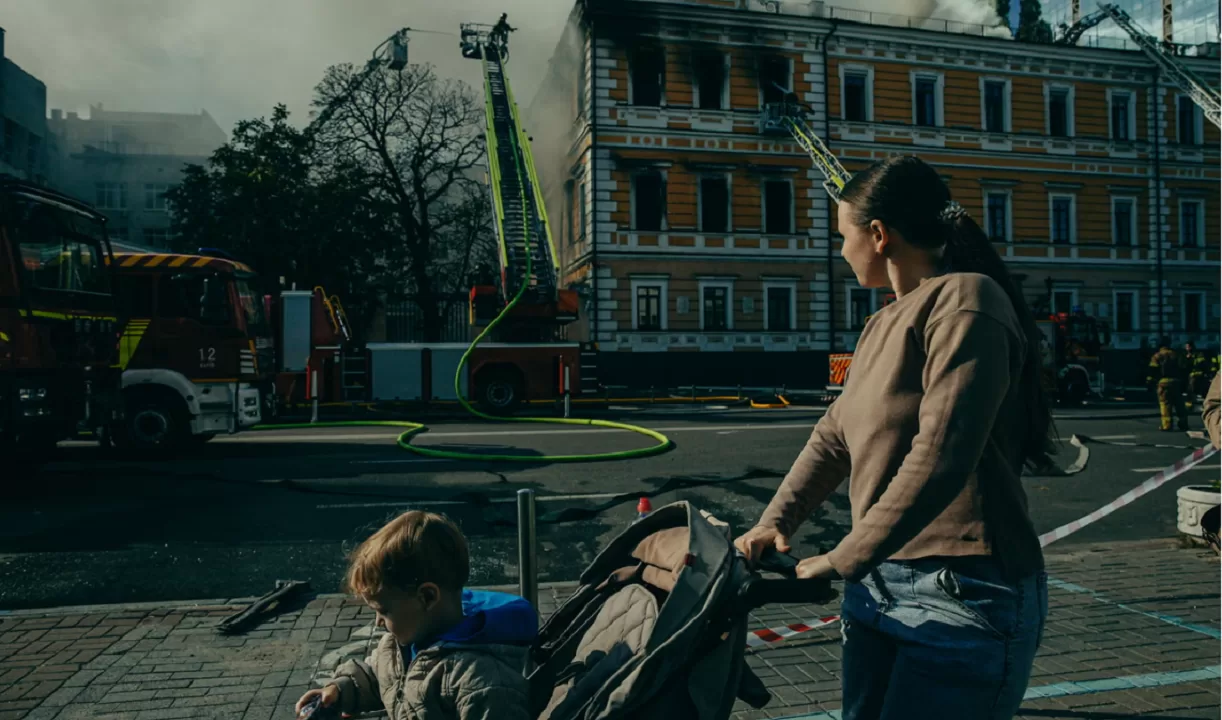 Жінка з дитиною проходить повз будівлю в Києві, де рятувальники ліквідовують наслідки російського удару / Фото: Julia Kochetova/The Guardian