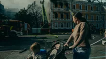 Женщина с ребенком проходит мимо здания в Киеве, где спасатели ликвидируют последствия российского удара / Фото: Julia Kochetova/The Guardian