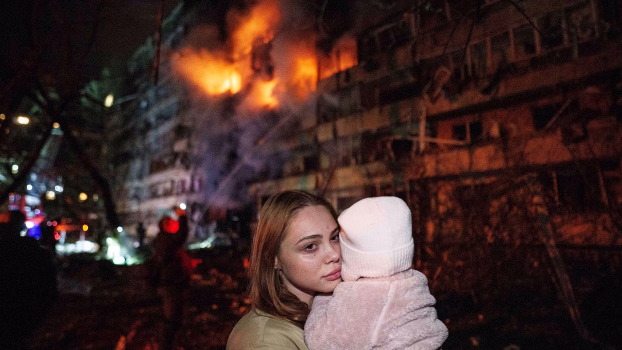 Женщина держит дочь возле жилого дома, поврежденного в результате российского ракетного удара по Киеву / Фото: Евгений Малолетка / AP
